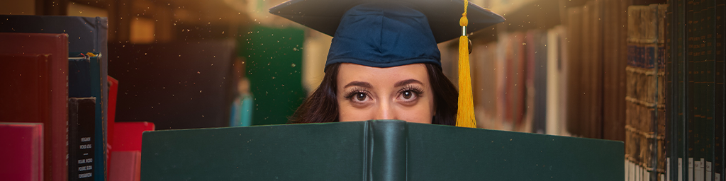 Undergraduate woman student holding a very large book and looking over the top in a library