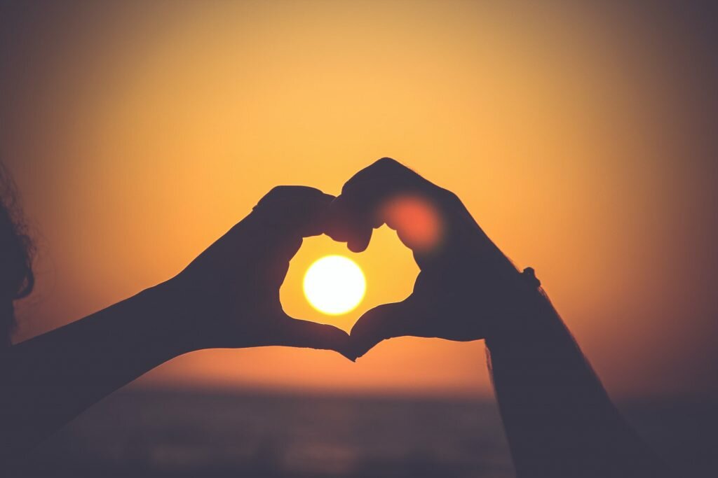 Two hands make the shape of a heart around the sun low in the sky