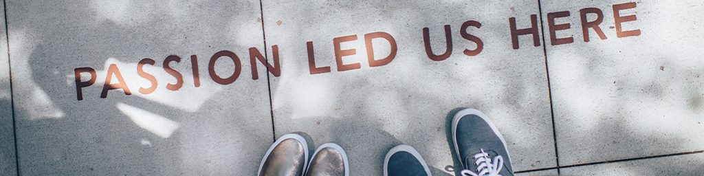 The words 'passion led us here' on a pavement with the shoes of two people looking at it